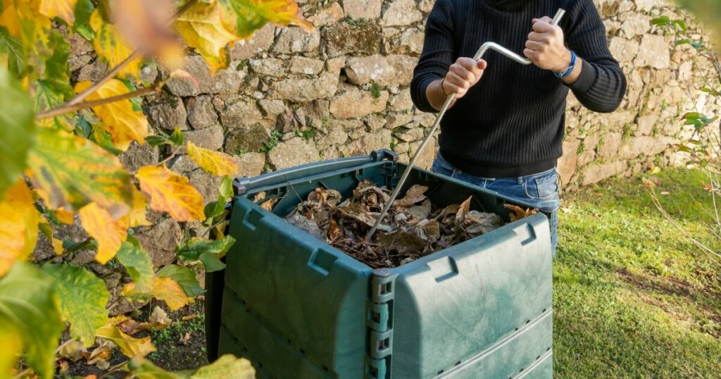 gardener aerating compost bin with tool