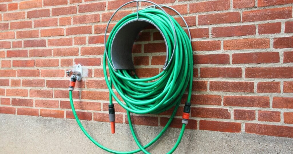 green garden hose stored on side of house